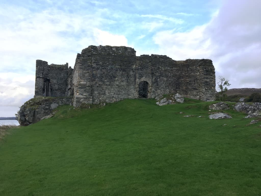 Historic ruins of Castle Sween in Scotland, overlooking a green hillside with cloudy skies in the background. One of Scotland's oldest stone castles, representing ancient Scottish architecture and heritage.