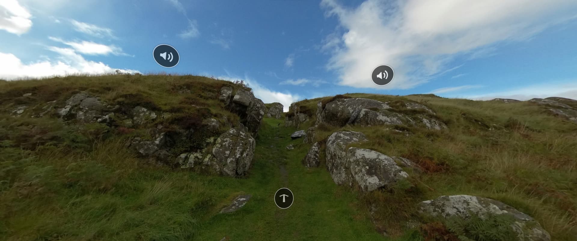 Pathway leading through rocky terrain up Dunadd Hillfort in Scotland, with grassy hills and a blue sky. Historic site known for its significance in ancient Scottish history and the Kingdom of Dalriada